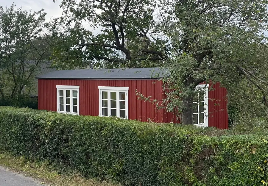 Penalhuset i falurød bag en klippet hæk